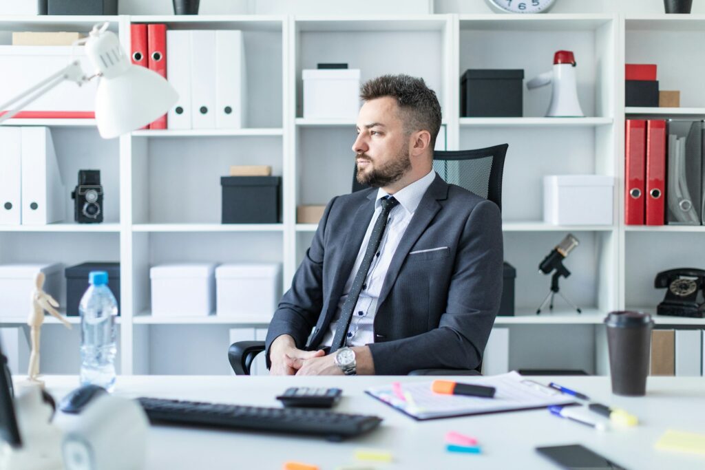 A man is sitting in a chair in the office at the table.