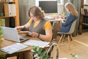 Young disable manager in casualwear sitting in wheelchair in front of laptop