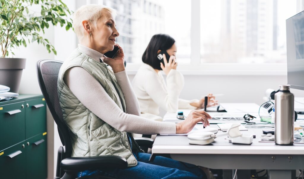 adult female entrepreneur phoning via mobile gadget talking at desktop