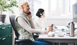 adult female entrepreneur phoning via mobile gadget talking at desktop